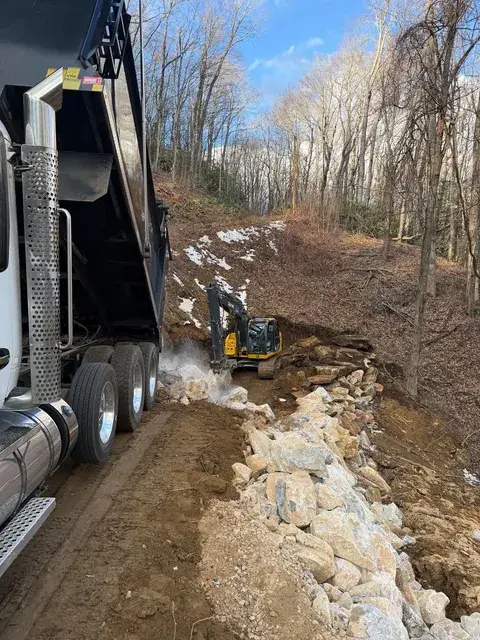 A dump truck and excavator placing rock on a slope