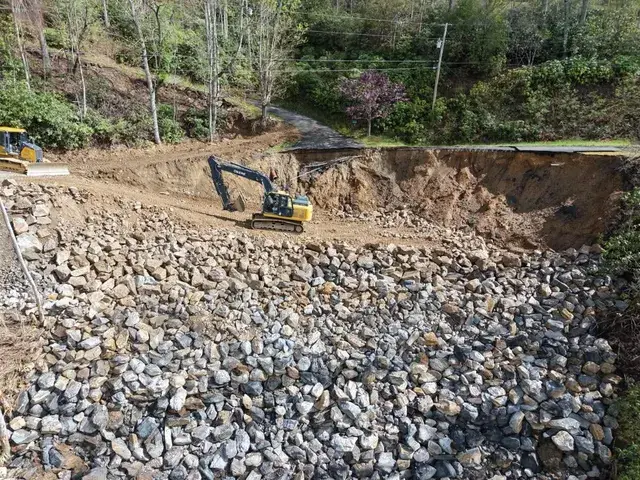 An excavator on a stone-covered site cut into a hillside