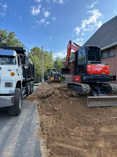 An excavator and dump truck working beside a paved drive