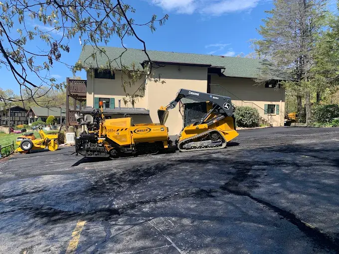 A paver and track loader on a lot in front of a building