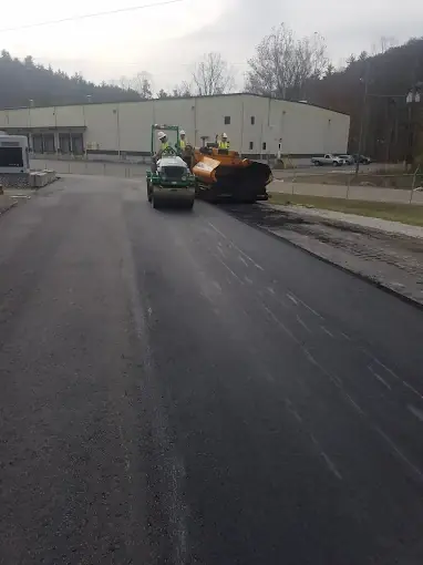 A paver and roller on a lot beside a large building