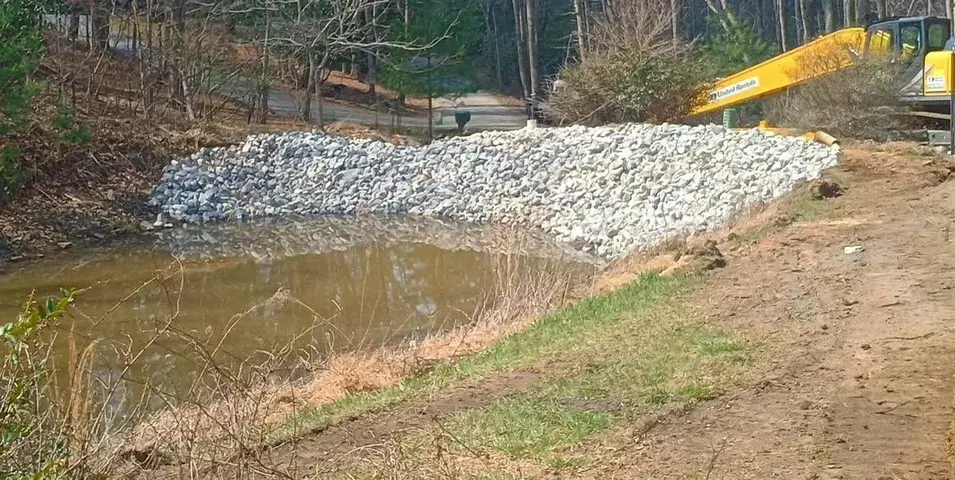 Riprap along a pond bank, with an excavator above