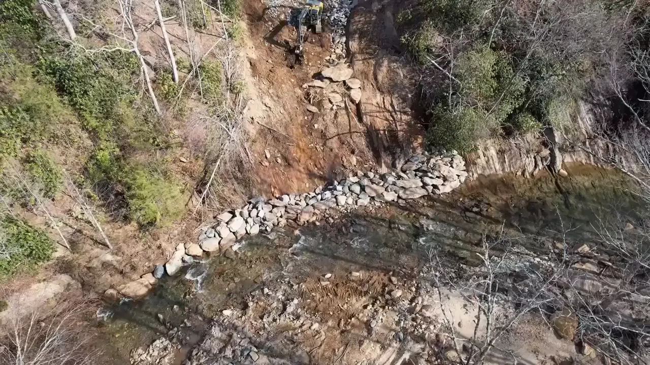A slid slope rebuilt with large rock, excavator at the top of the bank